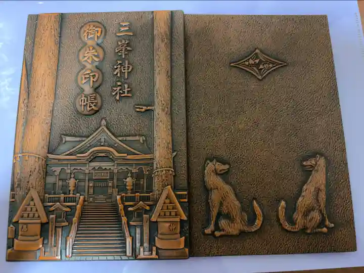 表紙が木彫りの凹凸でできており、表は社殿と御神木で裏が御眷属様